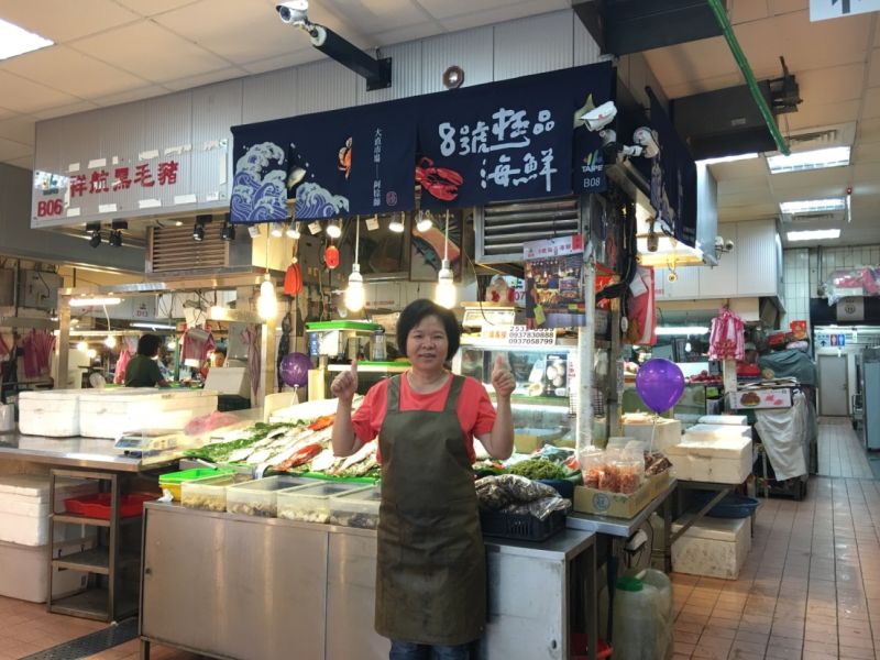 ▲設計師聶永真為海鮮店設計招牌，以布簾為主體，加上立體海鮮模型穿插，宛如海鮮正活跳地藏在布簾當中。圖為老闆娘開心與改造招牌合影。（圖／北市文化局提供）