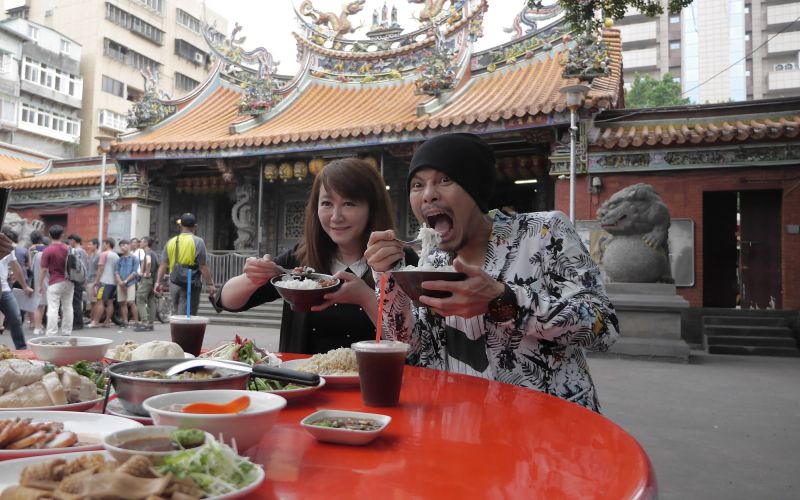 ▲黃明志拍台北市觀光宣傳影片並以臉書直播宣傳，台北市觀光傳播局局長簡余晏到大稻埕慈聖宮探班，準備滿桌古早味美食。（圖／北市觀傳局提供）