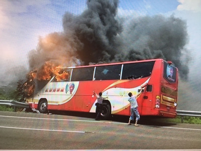 陸客團遊覽車19日中午在國道2號發生火燒車，第一時間試圖協助救援的國道泰山分隊員警林光華（左）及熱心砂石車司機（右）在靠近車尾處持滅火器猛敲車窗。（民眾提供）中央社記者卞金峰傳真  105年7月19日