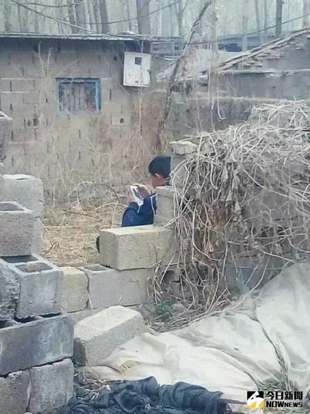 圖為一小學生在一廢棄的房屋旁邊坐著，手中緊握的是一部手機，此時的他正聚精會神的玩著「王者榮耀」，彷彿蹭上WIFI，世界與他無關。