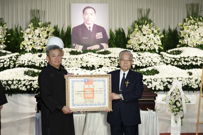 ▲ 故國防部物力司司長鄒弘達中將29日舉行追思告別式，前國防部長伍世文（右）代表頒贈旌忠狀給予家屬，表彰鄒將軍生前對國家的卓越貢獻。（軍聞社記者陳建興攝）