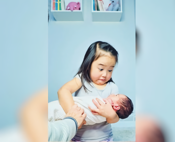 ▲網友分享女兒抱起新生妹妹的照片，女兒表情超母湯，笑翻大家。（圖／翻攝自 Reddit ）