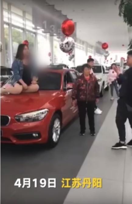 ▲一名灰色牛仔外套、黑色內衣、身材豐腴的女子坐在一輛紅色 BMW 展覽車引擎蓋上，聲嘶力竭的大聲叫囂。（圖／截自Youtube影片）