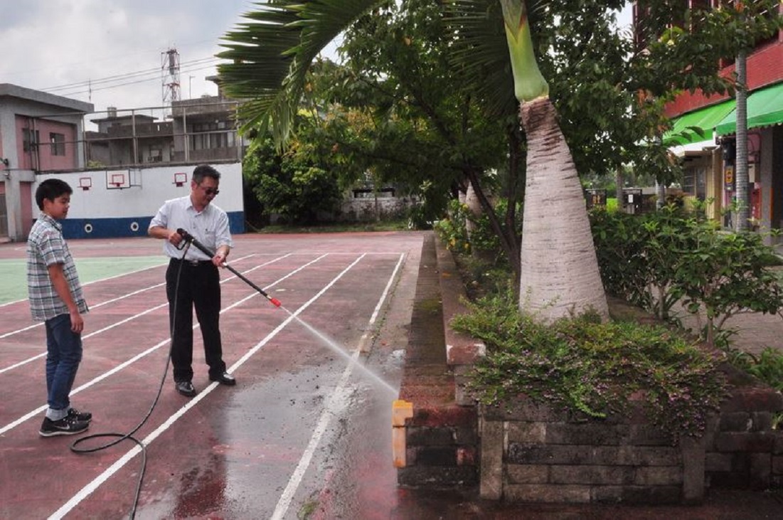 ▲新竹縣教育處長劉明超(右)示範「高壓強力清洗機」沖洗花台上附著的青苔、水溝及校園死角。（資料照片／新竹縣政府提供）