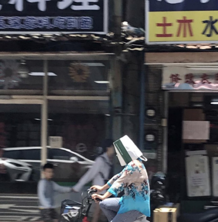 ▲近日有民眾在台北目擊，一名女子騎著腳踏車，直接將購物紙袋戴在頭上來防曬「擋日頭」，照片曝光，讓眾網友全都笑翻，直呼「這真是好主意...」。（圖／網友提供）