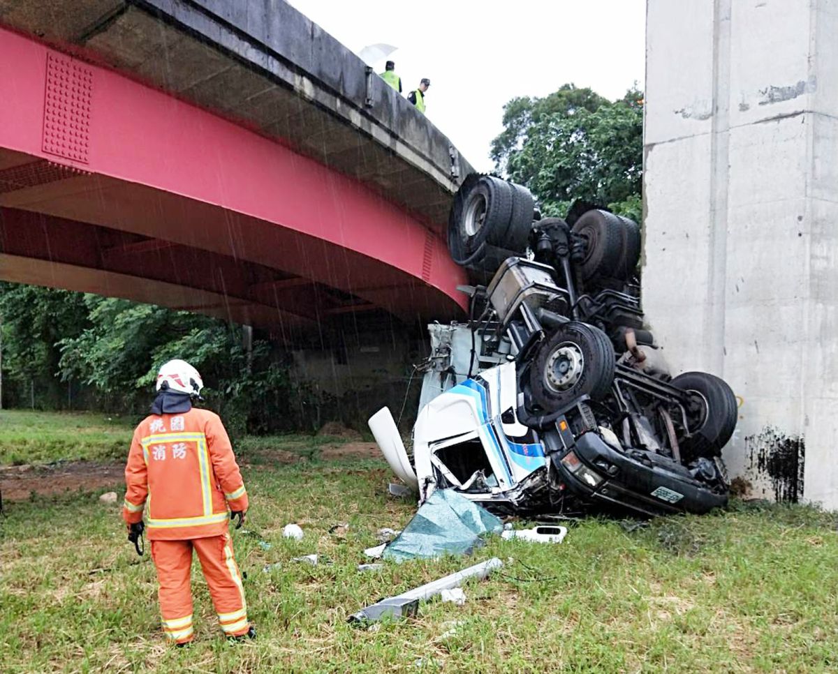 ▲貨櫃車在下閘道口時，疑似因為過彎速度過快，翻落橋下邊坡，造成車頭全毀，所幸駕駛命大逃過一劫。（圖／桃園市消防局提供）