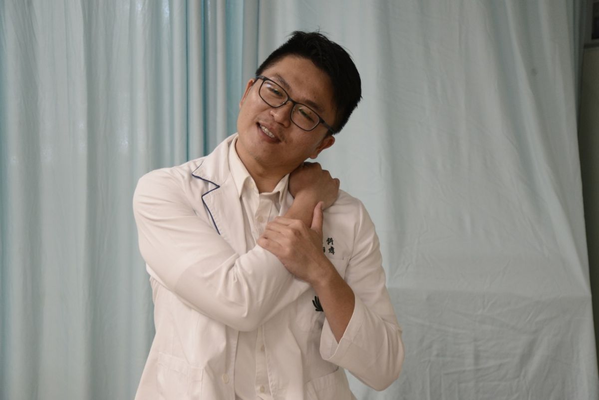 ▲鄭翔瑋物理治療師示範以對側手壓在落枕那一側的肩膀上，再以另一手輔助施力，向前、向下加壓，約10至15次，有助緩解症狀。（圖／大林慈濟醫院提供）