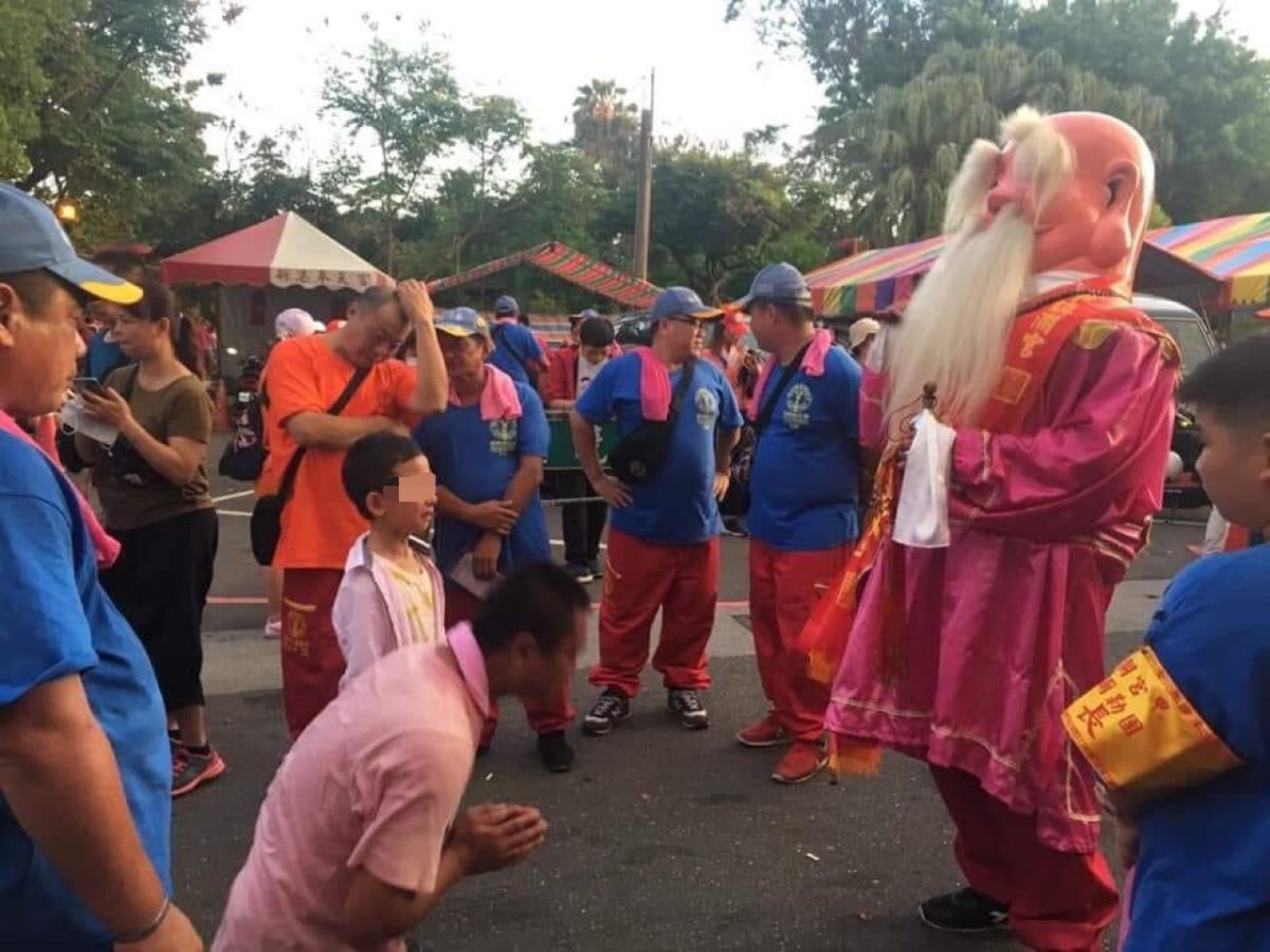 一對父子在烈日下祈求神明為家人治病。（圖／大甲鎮瀾宮福德彌勒團授權）