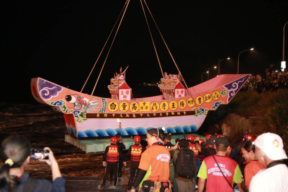 ▲各姓宗親會接序藉用大型吊車，把承載水燈頭的紙糊大型王船，慢慢放進海面。（圖／基隆市政府提供）