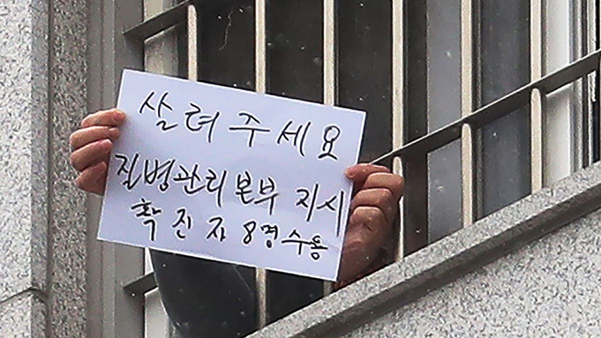 ▲首爾東部看守所內的囚犯，手拿字紙試圖向外求救「請救救我們，一間房就容納了8名確診患者」。（圖／翻攝自影片）