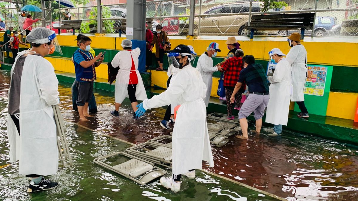 ▲那瑪夏區施打疫苗的籃球場接種站因持續性大雨，造成場地積水約5公分高，原民會及區公所同仁立即應變，利用鐵椅搭建人工走道，攙扶長者移至民權教會施打疫苗。（圖／高雄市原民會提供）