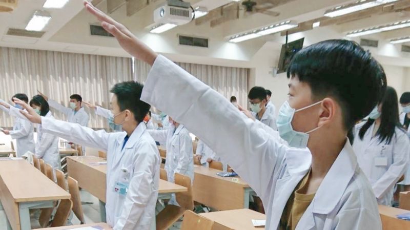▲學員身披白袍，高舉右手，宣讀醫學教育誓詞。（圖／高醫大提供）