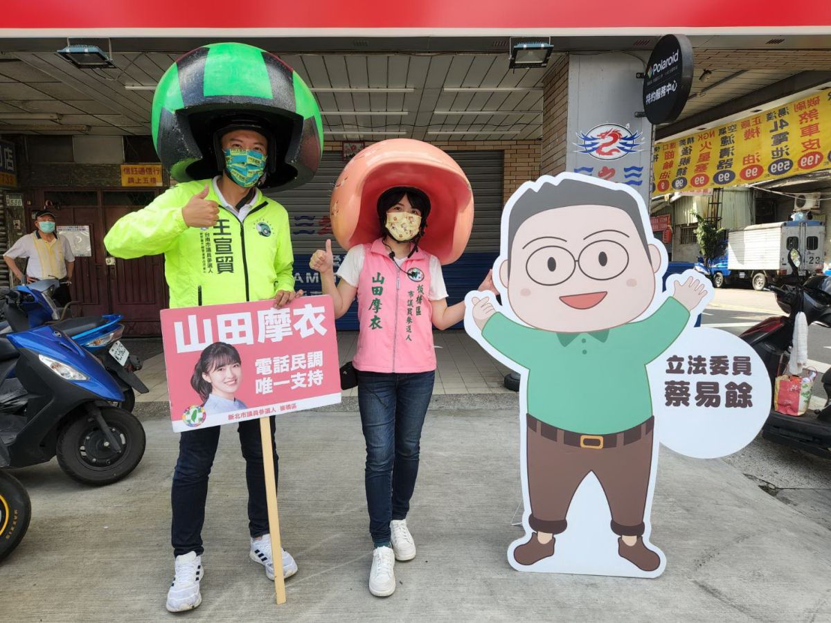 ▲山田摩衣在立委蔡易餘Q版人形看板的陪痛下，與王宣貿戴上各具自己特色的巨型安全帽，向上班的民眾揮手致意。（圖／山田摩衣提供）