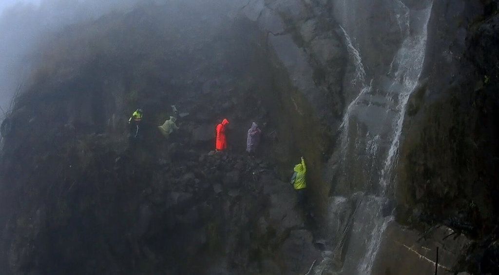 ▲阿里山林鐵眠月線一處隧道崩塌處因15日降雨形成水瀑，3名登山客受困待援，嘉義縣阿里山消防分隊人員趕往救援，待雨勢停，水瀑減緩，立即以人力接駁方式協助3人脫困，均無受傷。（嘉義縣消防局提供）