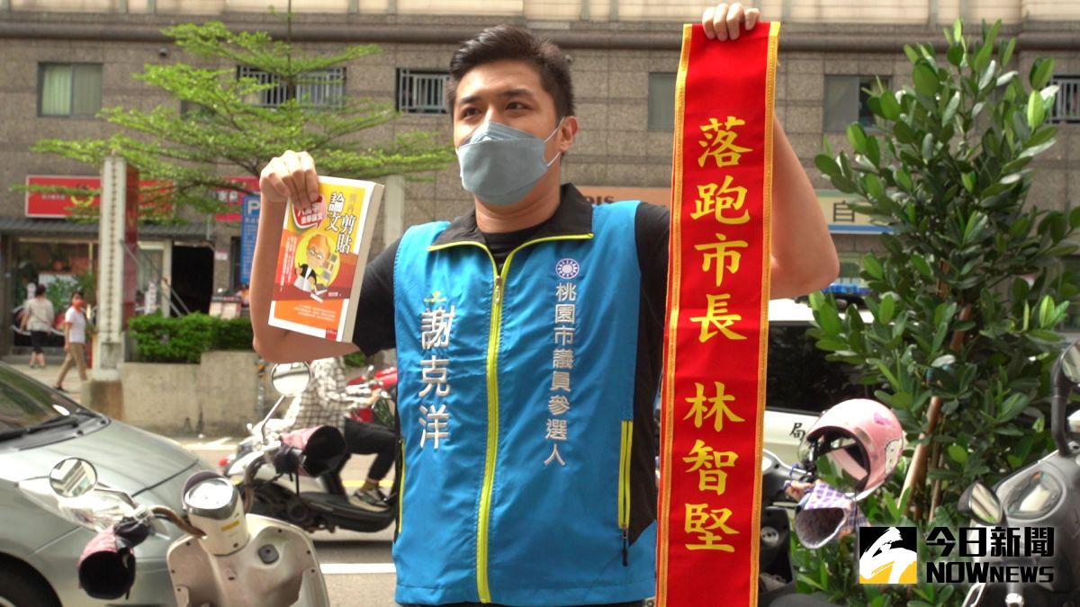 ▲林智堅成為桃園市民的第一天，藍營市議員參選人謝克洋拿著「別再剪貼論文」的書和印著「落跑市長林智堅」的紅色彩帶，要林收下這兩份禮。（圖／記者李春台攝，2022.07.12）