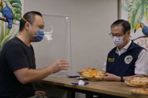 ▲香港籍新住民Howard（左）向移民署署長鐘景琨（右）介紹「一個人的披薩」。（圖／移民署提供）