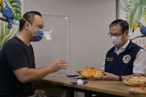 香港籍新住民Howard(左)向移民署署長鐘景琨(右)介紹「一個人的披薩」。(圖/移民署提供) ▲香港籍新住民Howard(左)向移民署署長鐘景琨(右)介紹「一個人的披薩」。(圖/移民署提供)