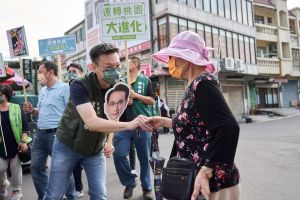 鄭運鵬日前確診,民進黨公職輪番到桃園,當起其分身拜票。圖為黨副秘書長林飛帆拿著鄭運鵬頭像看板,於大園市場向市民問候。 ▲鄭運鵬日前確診,民進黨公職輪番到桃園,當起其分身拜票。圖為黨副秘書長林飛帆拿著鄭運鵬頭像看板,於大園市場向市民問候。(圖/鄭運鵬辦公室提供)