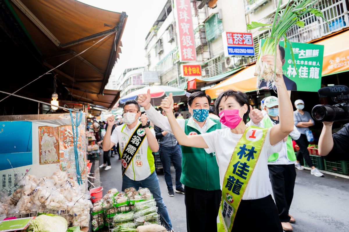 ▲鄭麗君背上林佳龍的競選背帶，代替確診的學長到新莊裕民市場掃街拜票。（圖 ／林佳龍競選辦公室提供）