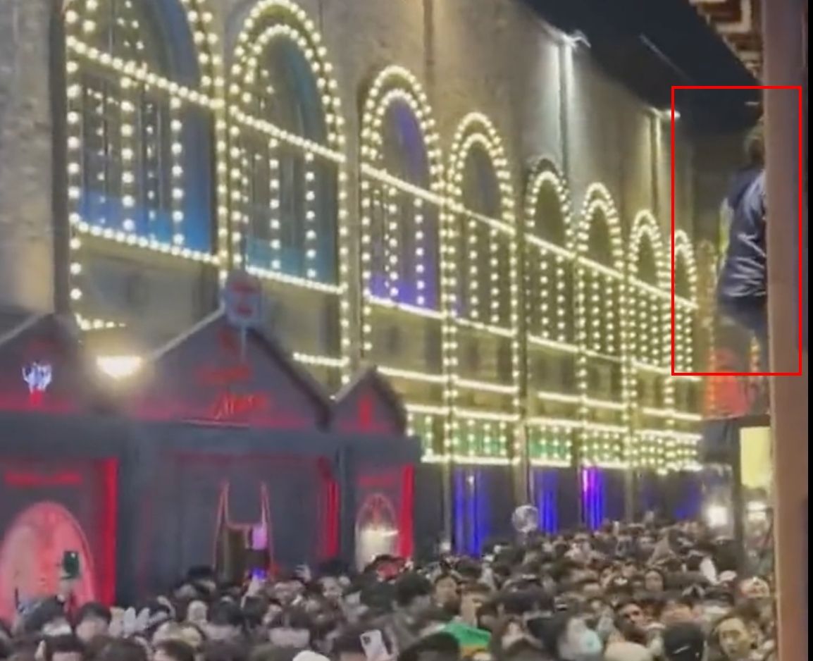 ▲梨泰院日前發生大規模踩踏傷亡事件，一名金髮男為求自保，直接爬上店家招牌上逃生。（圖/Twitter@sirajnoorani）