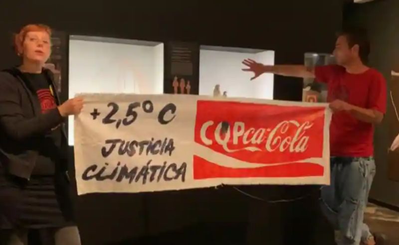 ▲氣候變遷抗議人士13日又在西班牙巴塞隆納的埃及博物館，用紅色和咖啡色膏狀液體潑灑玻璃櫃，又各將一隻手黏在展示櫃上，並舉起一個修改過的可口可樂布條。（圖／翻攝自法新社）