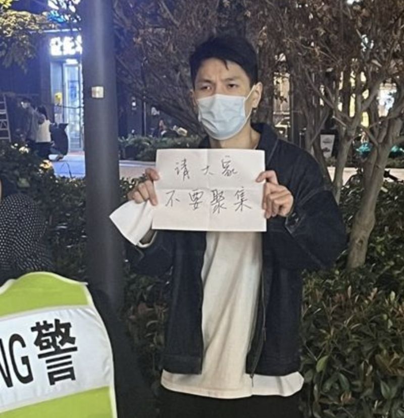 ▲一名男子手拿白紙以外,上頭還寫著「請大家不要聚集」的字眼,讓員警無可奈何。(圖/推特)