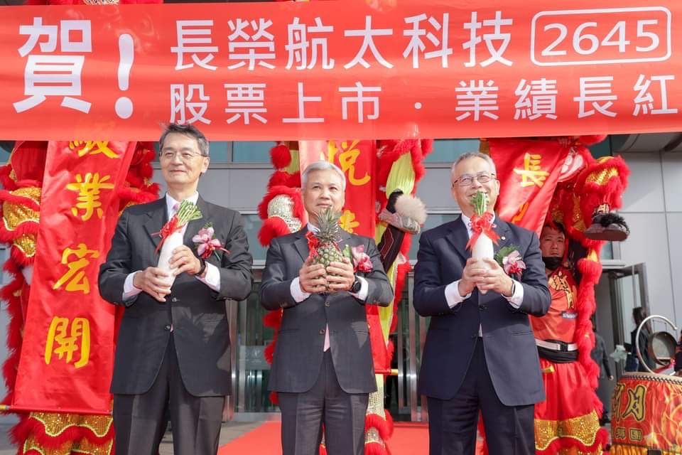 ▲長榮航太今（14）日掛牌上市，在舞獅表演中由董事長黃南宏（中）接下鳳梨，象徵事業旺旺，由維修事業體郭勝義總經理（右）、製造事業體總經理李緯章（左）接下象徵好彩頭的菜頭。（圖／長榮航太提供）