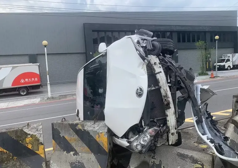 ▲一輛白色豐田汽車撞上中央分隔島「90度側翻」，前保險桿已脫落在地，但駕駛卻失去蹤影。（圖／翻攝畫面）