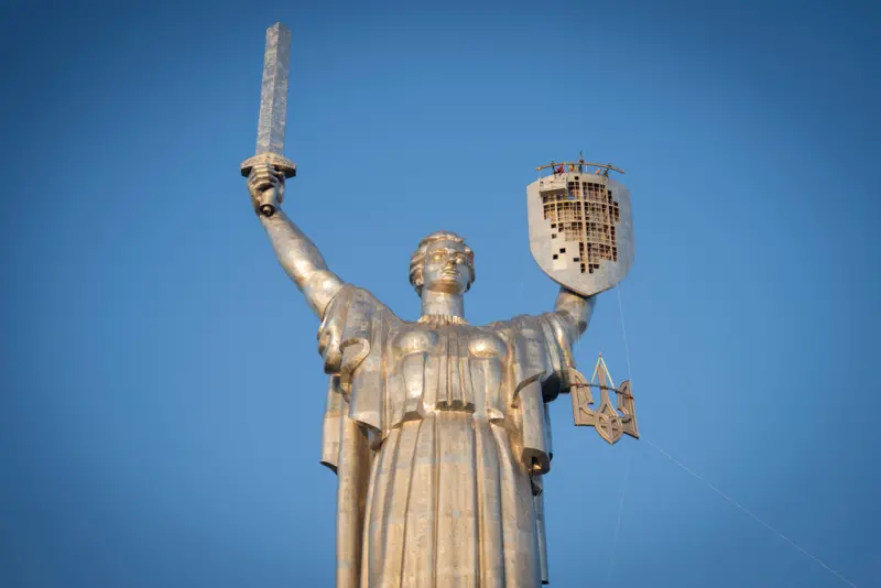 ▲烏克蘭的三叉戟國徽今天在首都基輔（Kyiv）一座巨大雕像的盾牌上閃爍著光芒，建築工人稍早將這個標誌以起重設備吊裝上烏克蘭最高的紀念碑，取代蘇聯的鐵鎚與鐮刀。（圖／美聯社／達志影像）