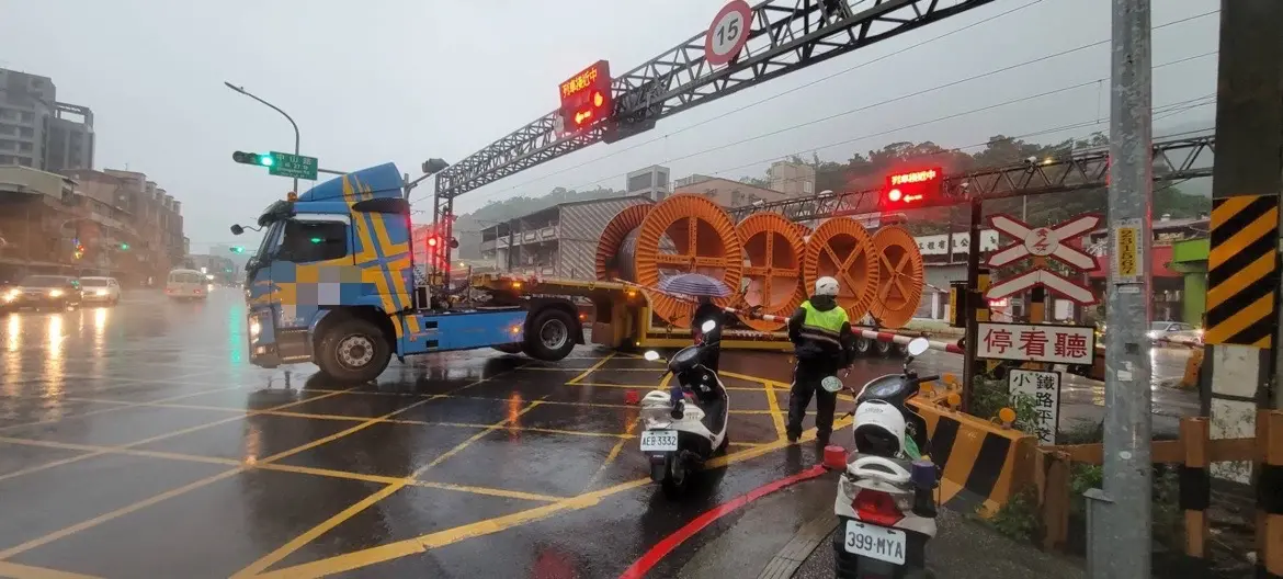 ▲負載電纜線的拖板車行經平交道，後輪卡在鐵軌間，雙線有火車即將經過，情況危急。（圖 ／翻攝畫面）