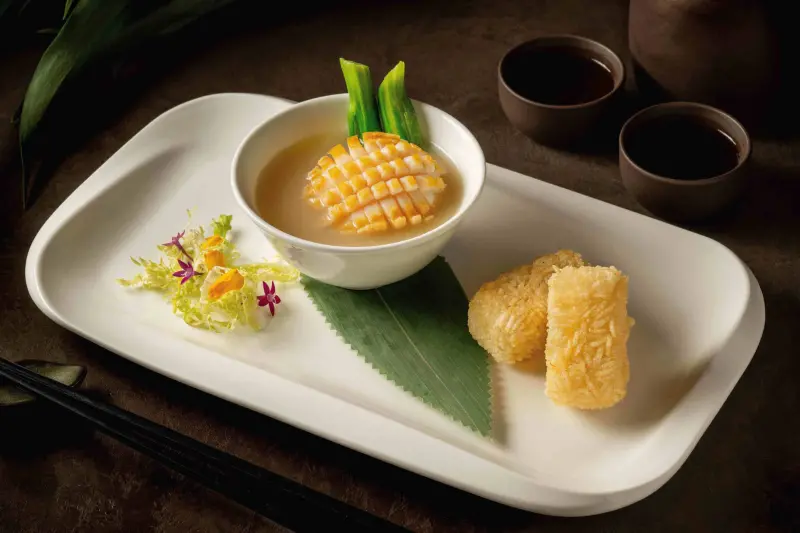 ▲「魚湯原粒鮮鮑炸飯糰」以繁瑣工序燉煮出的魚湯呈現奶白色,上頭還有花刀顆出漂亮外型的原粒鮑魚。(圖/台北香格里拉遠東提供)