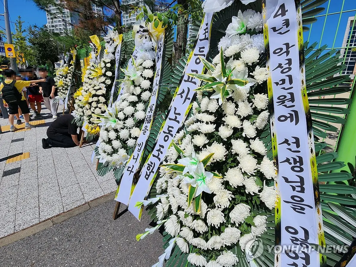 ▲韓國一名年輕教師今年7月初在學校輕生後，類似案例不斷爆出，教師權力低落問題開始受到社會關注。圖為另位輕生女教師任教的學校門口有民眾放上花圈哀悼。（圖／翻攝自韓聯社）