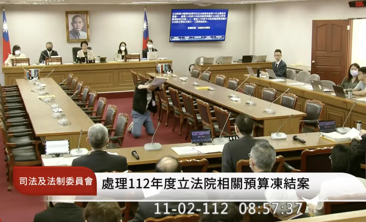 ▲今（2）日上午，立法院司法及法制委員會開會前，突然有一名身穿黑外套、牛仔褲，自稱為立法院公報處職員的男子走入會議室，看到秘書長林志嘉後，立即下跪用膝蓋走路，雙手高舉過頭遞交陳情書。（圖／翻攝國會頻道YT）