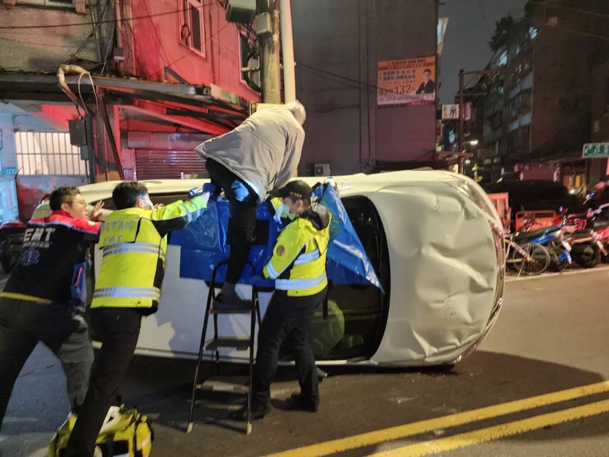 ▲白色小轎車失控撞上路旁車輛側覆橫立在馬路上，駕駛透過附近店家提供的板凳及梯子爬出。（圖 ／翻攝畫面）