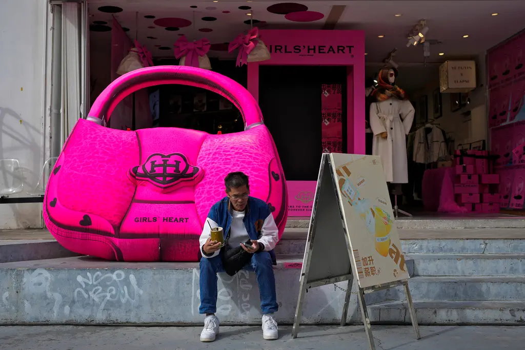 ▲中國社交平台近來公告從嚴打擊炫富拜金。圖為一名中國男子坐在精品名牌展示品前。（圖／美聯社／達志影像）