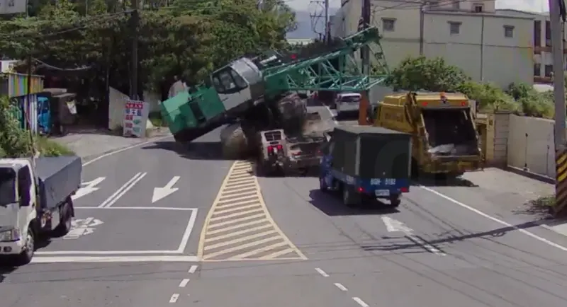 ▲林口一部拖板車行經彎道時，後方載運的吊車突然滑動向左傾斜，意外砸中路邊垃圾車。（圖／翻攝畫面）