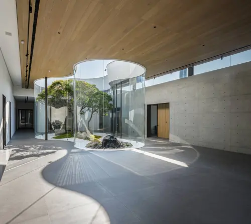 ▲鉅虹綠美館為開放式藝廊，中庭蓊鬱⼤樹以天井概念，⽤波浪型透明帷幕框起，讓綠蔭自然穿透。(圖／鉅虹提供）