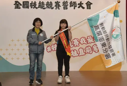 ▲勞動部勞動力發展署高屏澎東分署副分署長柯秀燕(左)授旗給代表機電整合職類出賽的選手陳奕婧(右)。(圖/勞動部高屏澎東分署提供) ▲勞動部勞動力發展署高屏澎東分署副分署長柯秀燕(左)授旗給代表機電整合職類出賽的選手陳奕婧(右)。(圖/勞動部高屏澎東分署提供)