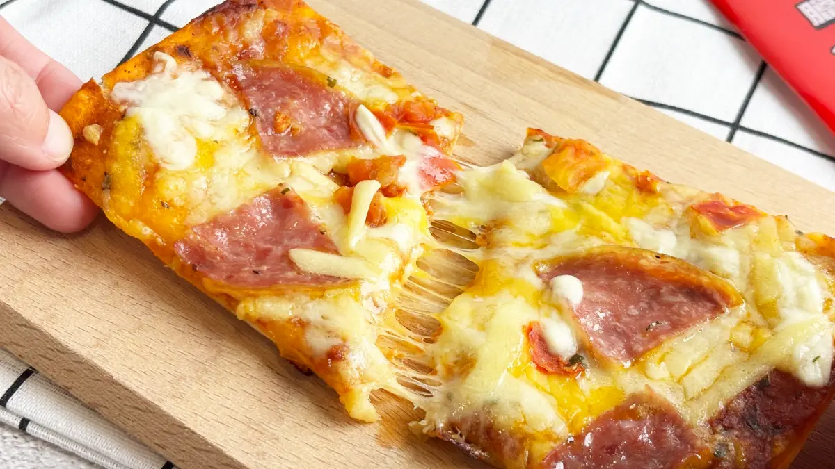 ▲Q彈有嚼勁的餅皮，抹上番茄醬，濃濃莫札瑞拉起司和鹹香多汁的美式臘腸。（圖／翻攝畫面）