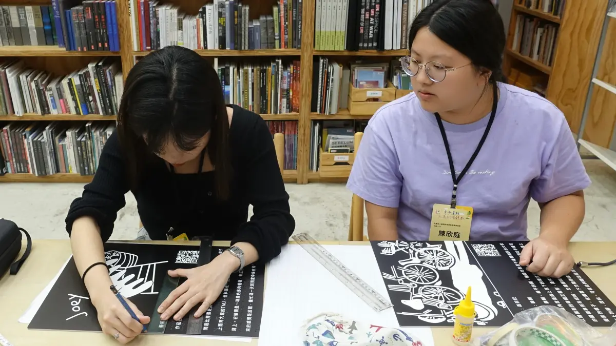 ▲陳欣庭同學(右)與曹孟涵同學(左) 進行實體展覽佈置，黏貼展覽海報。（圖／翻攝畫面）
