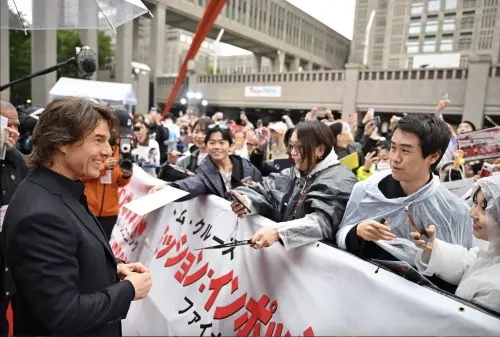 ▲湯姆克魯斯（左）為紅毯兩旁的粉絲簽名，活動一開始本來還下雨，有人幫他撐傘，粉絲身上也穿雨衣，但進行到一半雨就停了。（圖／UIP提供）