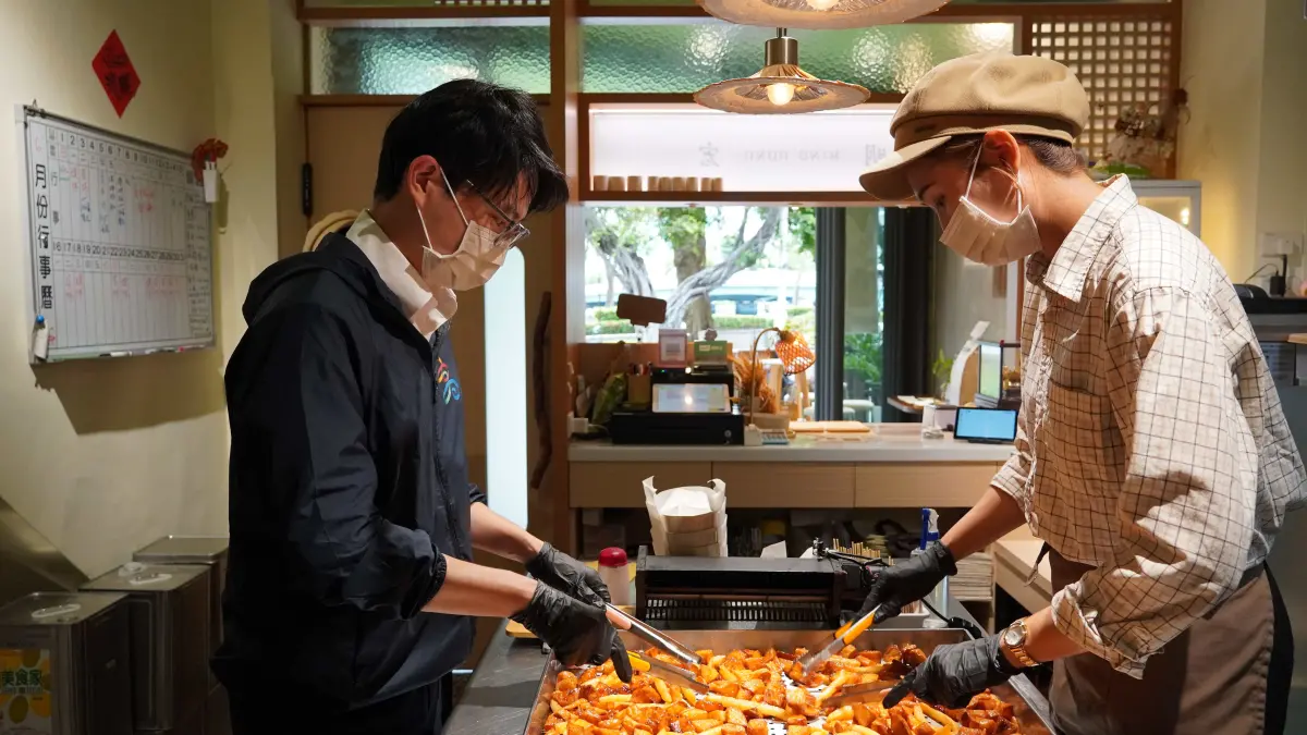 ▲高市青年局長林楷軒（左）實地走訪「明宏拔絲地瓜」，體驗翻炒拔絲地瓜的製作流程，感受傳統甜食背後的用心與傳承。（圖／高市青年局提供）