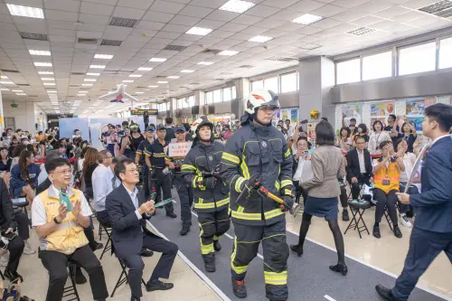 ▲高雄國際機場啟用60週年舉辦「飛安 Runway秀—公益闖關園遊會」，機場消防隊等駐站單位同仁化身模特兒，手持飛安標語牌，走上伸展台。（圖／高雄國際航空站提供）