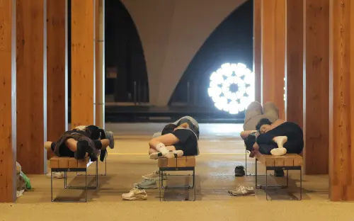 ▲被困在大阪世博會場的遊客只能躺在長椅上睡覺，或是在大屋頂環下的長椅休息。（圖／美聯社／達志影像）