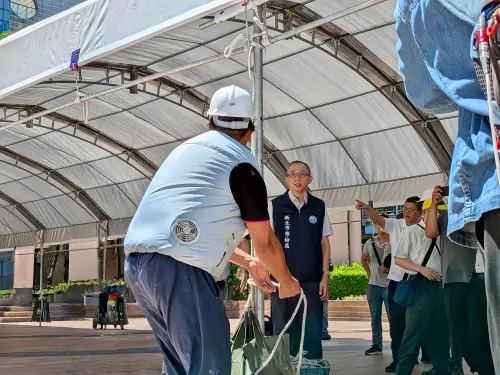 ▲在廣場搭棚架的韋成舞台結構的莊宇喬和夥伴體驗風扇衣，表示：「穿著(風扇衣)工作確實有變涼。」（圖／新北市勞動檢查處提供）