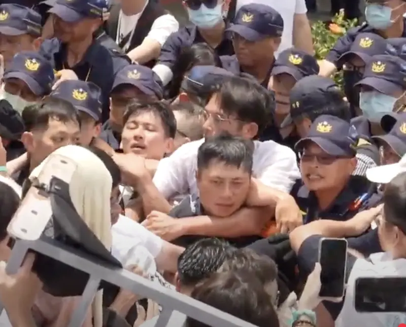 ▲民眾黨走讀與警方爆衝突，黃國昌翻過柵欄後，被困在員警陣中，疑似用手勒住員警脖子。（圖／翻攝自民眾黨直播）