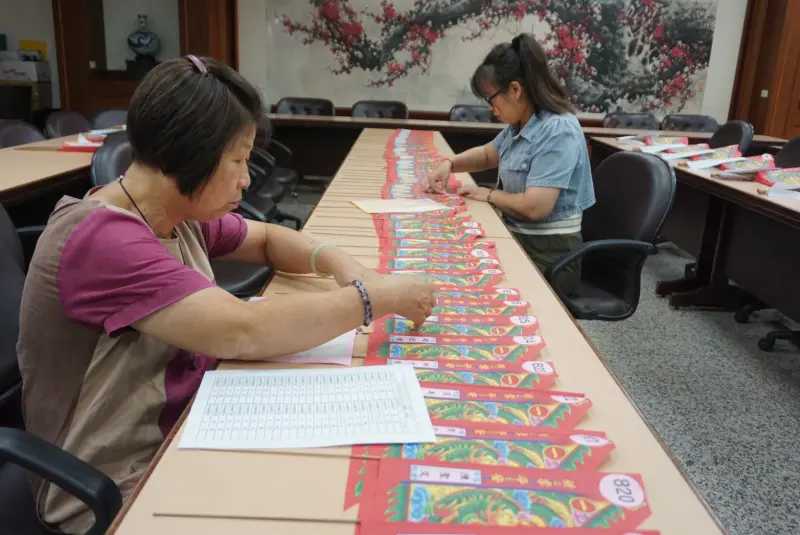 ▲萬和宮事務人員整理、黏貼普度旗編號及信眾姓名，進行先期作業。（圖／萬和宮提供）