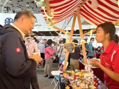 ▲高雄市政府勞工局局長江健興(左)巡視身心障礙職訓班學員成果展攤位，與學員(右)互動熱絡。(圖／高雄市政府勞工局提供)