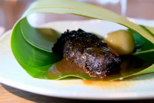 ▲AKAME以雲林「農場晃晃 Farm Around You」的牛肉做出三吃，圖為低溫慢烤牛小排以月桃葉包裹上桌。（圖／記者葉盛耀攝）