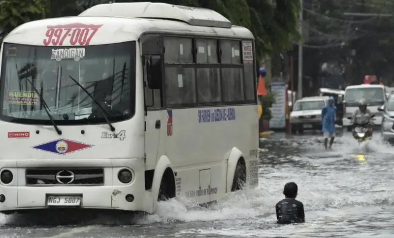 ▲豪雨導致馬尼拉交通癱瘓，公車與機車在積水道路艱難行駛，孩童甚至浸泡在水中，顯現都市治水問題的嚴峻。（圖／美聯社／達志影像）
